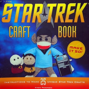 May include: The Star Trek Craft Book cover shows a sock monkey in a Starfleet uniform, with the Star Trek logo above. The book contains instructions to make 25 unique Star Trek crafts. The cover has the text "Make it so!"