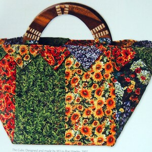 May include: A patchwork tote bag with a wooden handle. The bag is made of fabric with a floral pattern in shades of red, green, yellow, and purple. The text "The Cube. Designed and made by M. Liss Rae Hawley, 2007" is printed at the bottom of the image.