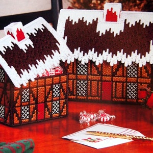 Puede incluir: Dos cajas decorativas con forma de casa de jengibre con tejados blancos cubiertos de nieve y chimeneas rojas. Las casas son marrones con adornos blancos y presentan pequeñas ventanas y puertas rojas. También se ve un muñeco de nieve y caramelos.