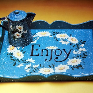 May include: A blue wooden tray with a white daisy design and the word "Enjoy" painted on it. A blue teapot with a white daisy design is on the tray.
