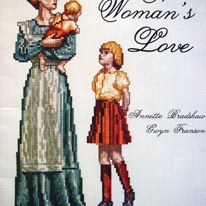 Puede incluir: Un patr&oacute;n de bordado de punto de cruz contado que representa a una mujer sosteniendo a un ni&ntilde;o y una ni&ntilde;a de pie a su lado. El dise&ntilde;o se titula "A Woman's Love" e incluye los nombres Annette Bradshaw y Gwyn Franson. El patr&oacute;n se describe como "Bordado de punto de cruz contado con "The Personal Touch."