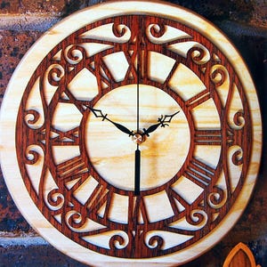 Può includere: Un orologio in legno con una cornice in legno marrone e un quadrante bianco. L'orologio ha numeri romani e una lancetta delle ore e dei minuti nera. L'orologio è circondato da un design decorativo.
