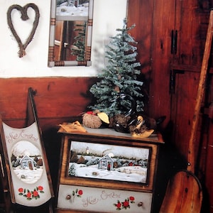 May include: A wooden chest with a painted scene of a snowy New England village. The chest has a drawer with a painted scene of a lighthouse and the words "New England" written on it. The chest is decorated with a heart-shaped wreath and a mirror with a painted scene of a house. The text "The New England Seaside" is written on the wall above the chest. The text "Mirror, Sled, Chest" is written below the text "The New England Seaside". The text "Instructions begin on page 25." is written below the text "Mirror, Sled, Chest".