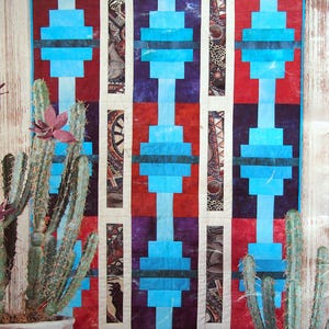 May include: A Southwestern-style quilt with a geometric pattern in shades of blue, red, and white. The quilt is made up of squares and rectangles, and the pattern is repeated throughout the quilt. The quilt is framed by a white border.
