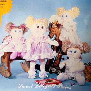 May include: Four handmade dolls with yarn hair and embroidered faces. Two dolls are seated on a wooden rocking horse. The dolls are wearing pink dresses with lace trim. The text "Sweet Delights Series" is at the bottom.