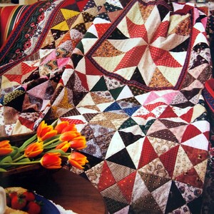 May include: A colorful patchwork quilt with a starburst pattern in the center. The quilt is made of various fabrics in shades of red, brown, white, and green. The quilt is draped over a couch with a floral pattern.