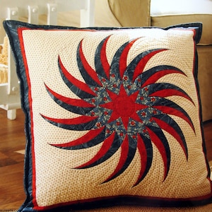 May include: A red, white and blue quilted cushion with a starburst design. The cushion is made of fabric with a small white polka dot pattern.