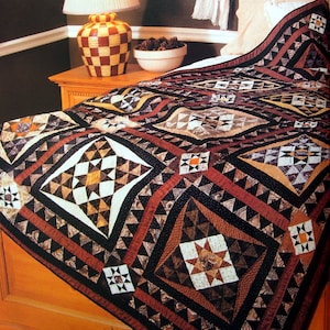 May include: A quilt featuring a geometric pattern in shades of brown, black, white, and orange. The quilt is made from various fabrics and has a star-shaped design in the centre.