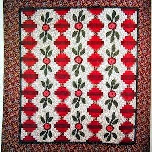 Op de afbeelding: Een rood en wit quilt met een herhalend patroon van groene bladeren en rode bloemen. De quilt is omzoomd met een bruin en wit bloemenprint.
