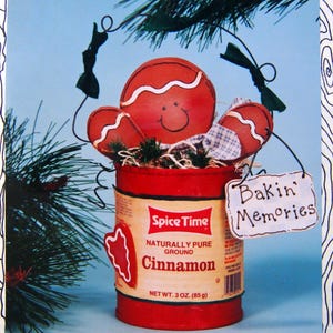 May include: A decorative gingerbread man figure with a smiling face, arms, and a red body, sits atop a red Spice Time cinnamon can. The can has a beige label with the words "Cinnamon" and "Bakin' Memories" on a small sign. Net weight is 3 oz (85 g).