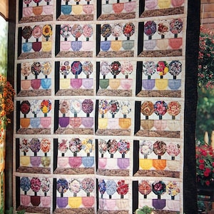May include: A handmade quilt with a repeating pattern of floral arrangements in colourful pots. Each arrangement has a unique flower design. The quilt has a neutral background with a dark border and is displayed outdoors.