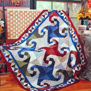 Peut inclure: Une courtepointe colorée avec un motif en spirale dans des tons de bleu, rouge et vert. La courtepointe est faite de tissu patchwork et a un fond blanc. Elle est drapé sur une chaise en bois avec un siège tissé.