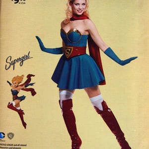 May include: A Simplicity sewing pattern for a Supergirl costume from DC Comics Bombshells. The costume features a blue dress, red cape, and thigh-high boots. The pattern includes sizes U.S. 14-22.