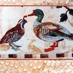May include: A fabric art piece titled "Feather & Song" featuring a Common Shell Duck and California Quail. The duck has green, brown, and white feathers, while the quail is brown with white spots. The artwork includes text and is signed by the artist.
