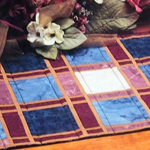 May include: A plaid table runner with a brown, white, blue and pink checkered pattern. The runner is made of fabric and has a slightly textured surface.