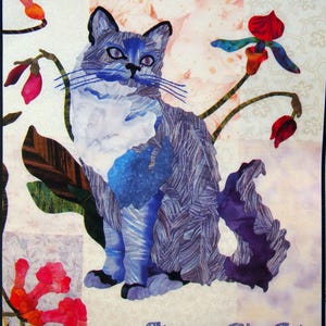 May include: A fabric art piece featuring a blue Birman cat with a white chest and blue eyes, surrounded by floral accents in red, green, and brown. The text "Birman - Blue Point" is at the bottom.
