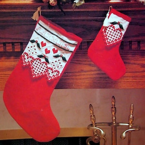 May include: Two red Christmas stockings with white and red embroidered details. One stocking has the name "MARIANN" embroidered on it. Both stockings have heart and holly designs.