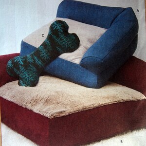 May include: A blue and beige dog bed with a bone-shaped pillow. The pillow is green with a white pattern. The bed has a red base.