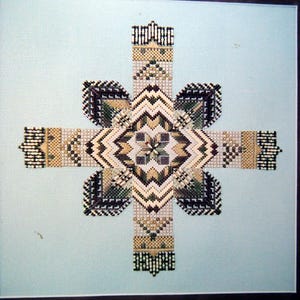 May include: A geometric cross-shaped needlepoint design. The artwork features a central diamond shape with a starburst pattern, surrounded by four petal-like shapes. The color palette includes shades of beige, green, black, and white, set against a light blue background.