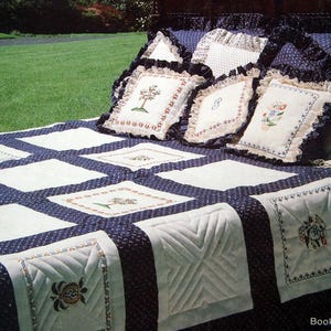 May include: A quilted bedspread and pillows with a navy blue and white color scheme. The bedspread features a grid pattern with embroidered squares. The pillows have embroidered designs and ruffled edges. The text "Book #8" is visible.