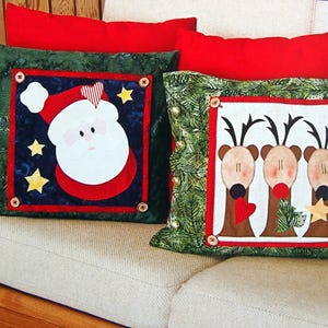 May include: Two Christmas-themed throw pillows. One pillow features a green background with a red, white, and blue Santa Claus applique. The other pillow features a green background with three reindeer appliques.