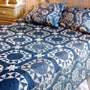 Könnte beinhalten: Ein blau-weißes Steppbett mit floralen und geometrischen Mustern bedeckt ein Bett. Zwei passende Kissen liegen auf dem Bett. Das detaillierte Design des Quilts schafft ein gemütliches und dekoratives Bettwäsche-Set.