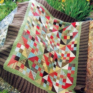 May include: A patchwork quilt with a geometric design in shades of brown, red, green, blue, and white. The quilt is made of various fabrics with different patterns and textures.