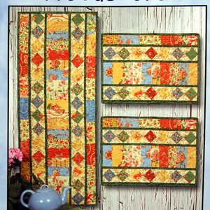 May include: Quilting pattern for a table runner and placemats. The pattern is called "Table Charm" and is charm friendly. The pattern includes a 15 inch by 40 inch runner and placemats. The pattern features a floral design with red, yellow, blue, and green colors.