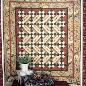 Op de afbeelding: Een quiltpatroon met een 9-patch ontwerp met een zwart-wit geruit patroon met rode en crème accenten. De quilt wordt getoond op een houten tafel met een bloemstuk ervoor. De tekst "9-Patch Side Step" is onder de quilt gedrukt.