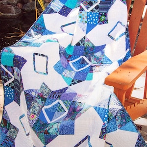May include: A patchwork quilt featuring a variety of blue, teal, and white fabric squares. The design incorporates geometric shapes, including diamonds and rectangles, with intricate stitching patterns throughout the textile surface.