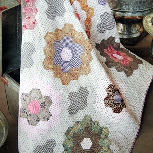 May include: A white quilt with a patchwork design featuring a variety of floral patterns in shades of pink, purple, brown, green, and yellow. The quilt is made with a variety of fabrics, including gingham, paisley, and floral prints. The quilt is quilted with a simple stitch pattern.