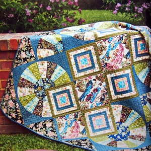 Peut inclure: Une courtepointe en patchwork bleu, vert et rose avec une variété de motifs et de designs. La courtepointe présente un motif circulaire central avec des rayons radiants, entouré de carrés et de rectangles avec des motifs floraux et géométriques.