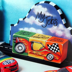 May include: A wooden race car toy with three blocks that say "Make Bed", "Do Homework", and "Take Bath". The blocks are painted in bright colors and have a checkered flag design. The race car is on a black track with a blue and white checkered background. The words "My Jobs" are written on the background.