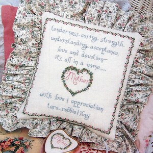 May include: A white pillow with a floral design and a cross-stitch design that reads "tenderness, caring, strength, understanding, acceptance, love and devotion, it's all in a name... Mother" with love & appreciation tara, robbie, kay.