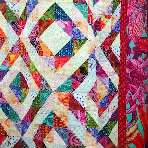 May include: A colorful quilt with a geometric pattern of triangles and squares. The quilt is made of various fabrics in shades of pink, red, green, blue, and white. The quilt is quilted with a white thread.