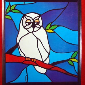 May include: Stained glass panel depicting a white owl on a red branch, with a blue backdrop and green leaves. The owl has brown eyes. The artwork is framed in black.