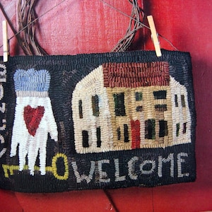 May include: A black and white welcome mat with a house design and a hand with a heart. The mat has the words "Welcome" and "1815-2018" on it.