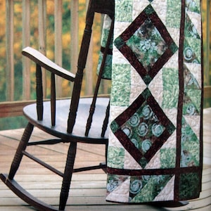 Peut inclure: Une chaise berçante avec une courtepointe verte et brune drapée sur le dossier. La courtepointe a un motif en losange sur fond blanc.