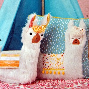 Puede incluir: Dos almohadas de peluche de llama blancas, una con un fondo estampado azul y blanco y la otra con una silla de montar a rayas amarilla y naranja. Ambas almohadas tienen una textura esponjosa blanca y rasgos faciales bordados.