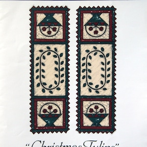 Puede incluir: Un camino de mesa de Navidad con un diseño acolchado con tulipanes rojos, verdes y crema. El camino de mesa se titula "Christmas Tulips" y "A Tulip Runner".