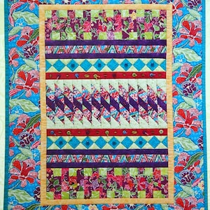 May include: A colourful quilt with a geometric pattern in the centre. The quilt is surrounded by a border of floral fabric with red, green and blue flowers on a light blue background.