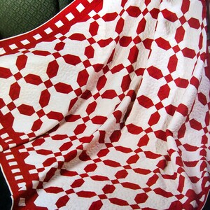 Peut inclure: Une courtepointe faite à la main avec un motif répétitif d'octogones rouges et de carrés blancs. La courtepointe a une bordure rouge avec des accents carrés blancs. Le tissu est plié, montrant la texture et le design de la courtepointe.