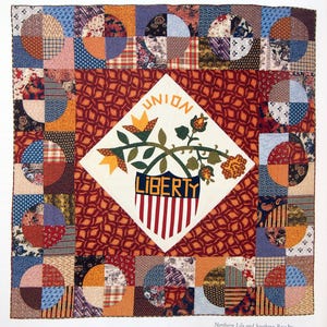 Puede incluir: Una colcha vintage con un panel central en forma de diamante que presenta un diseño floral estilizado y las palabras "UNION LIBERTY". La colcha está hecha de varias telas en tonos de rojo, blanco, azul y naranja, y está dispuesta en un patrón de patchwork.