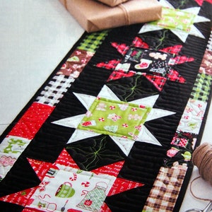 May include: A black and white table runner with a Christmas theme. The runner is decorated with red, green and white stars, and features a variety of festive fabrics. The text "Merry Christmas" and "Happy Holidays" is visible on the runner.