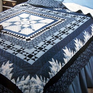 May include: A bed quilt featuring a central star pattern in shades of navy blue, light blue, and white. The design includes geometric borders with triangular and square motifs, finished with a dark blue floral print and solid navy blue fabric accents.