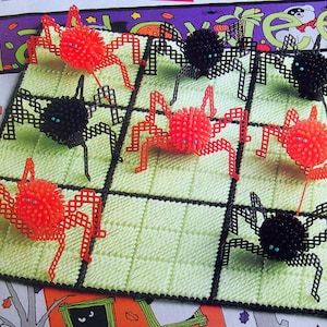 May include: A Halloween craft project showing a grid of spiders. The spiders are made of red and black plastic, with fuzzy pom-pom bodies and grid-like legs. The background is a light green grid, creating a festive atmosphere.