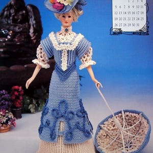May include: A handcrafted doll in a blue crochet dress, a matching hat with floral decorations, and a parasol. The doll has blonde hair and wears a high-collared dress with cream lace trim. A calendar for May 1996 is visible in the background.
