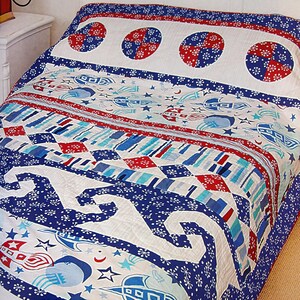 May include: A colorful quilt with a space theme, featuring rockets, stars, and geometric patterns in red, white, and blue. The quilt has a white background with blue and red accents, perfect for a bedroom.