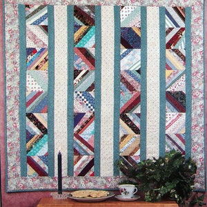 Op de afbeelding: Een quilt met een witte achtergrond en blauwe verticale strepen. De quilt is gemaakt van veel verschillende stofresten in verschillende kleuren en patronen. De quilt heeft de titel "Grandma's Strips".