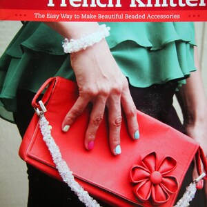 May include: A red clutch purse with a large red flower embellishment. The purse has a white beaded strap. The book cover text reads "Making Jewelry with a French Knitter. The Easy Way to Make Beautiful Beaded Accessories."